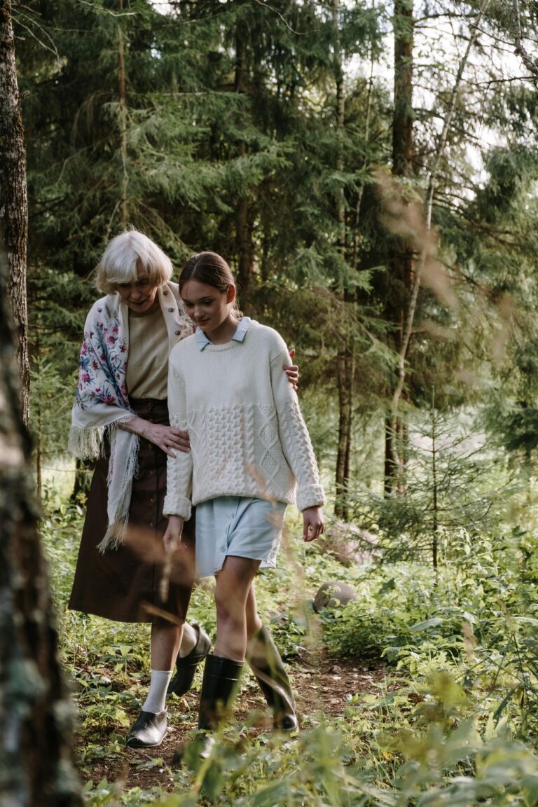 Elderly woman and young girl walking through lush green forest, sharing a peaceful moment.