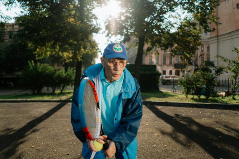A senior man playing tennis outside, enjoying leisure activities in the park during the day.