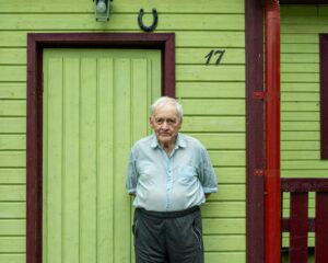 Senior man in front of vibrant wooden house in Tartu County, Estonia. Simple rural life portrait.