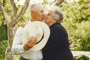 A loving elderly couple shares a tender kiss in a sunny garden, embracing each other warmly.