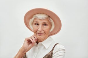 Portrait of an elegant senior woman wearing a stylish pink hat posing against a neutral background.
