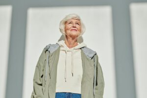 Portrait of a stylish senior woman in a coat and hoodie, embracing modern fashion outdoors.