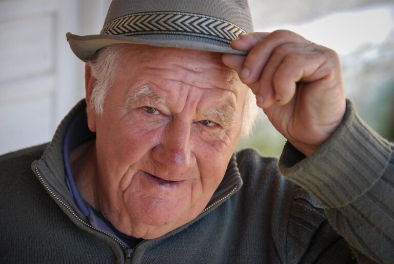 Portrait of a senior man smiling warmly while tipping his fedora hat, conveying charm and friendliness.