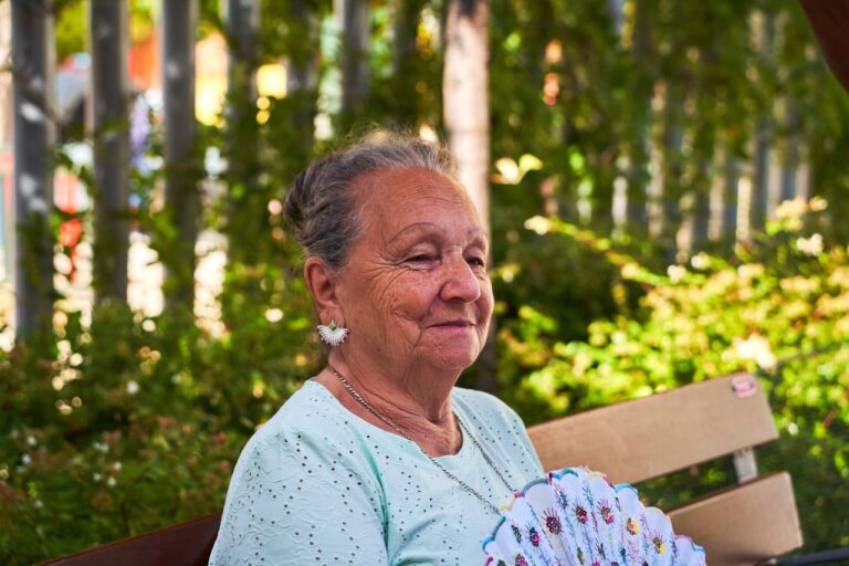 A senior woman enjoys a sunny day outdoors with a fan in San Sebastián de los Reyes, Spain.