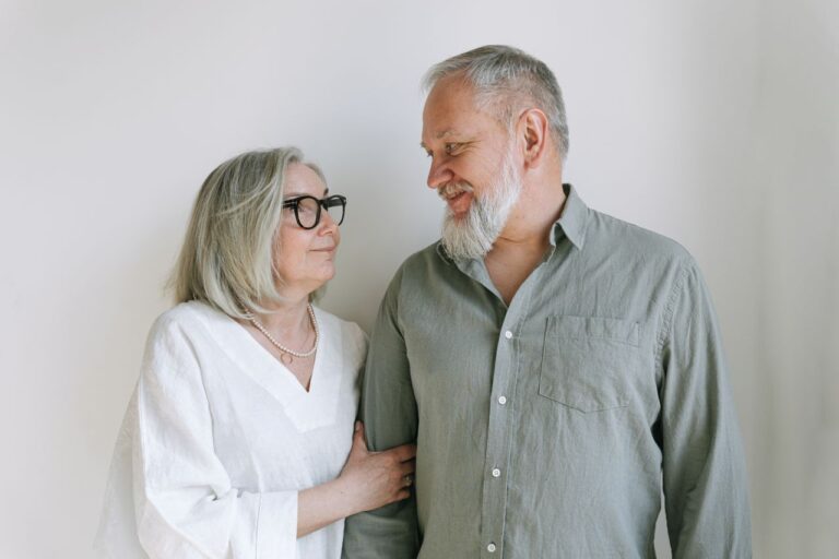Elderly man and woman smiling at each other with warmth and love indoors.