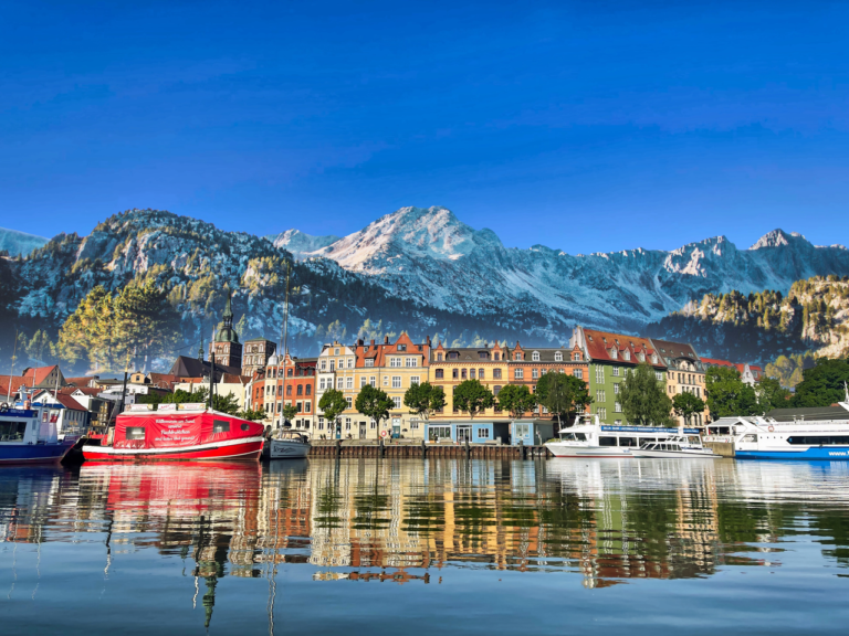 Picturesque view of Stralsund's charming harbor with dramatic snowcapped mountains and vibrant architecture.
